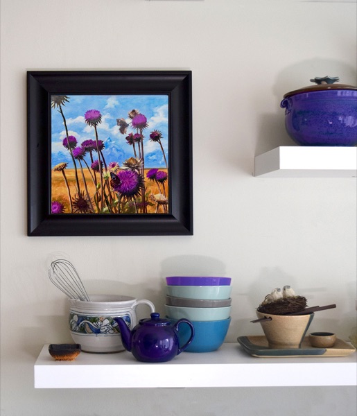 Teton Thistles framed on a wall above a shelf of colorful bowls and a purple teapot
