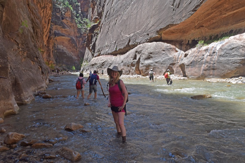 The artist with companions at a quiet bend of the Virgin River, hikers wading across the shallow current, canyon walls rising behind them